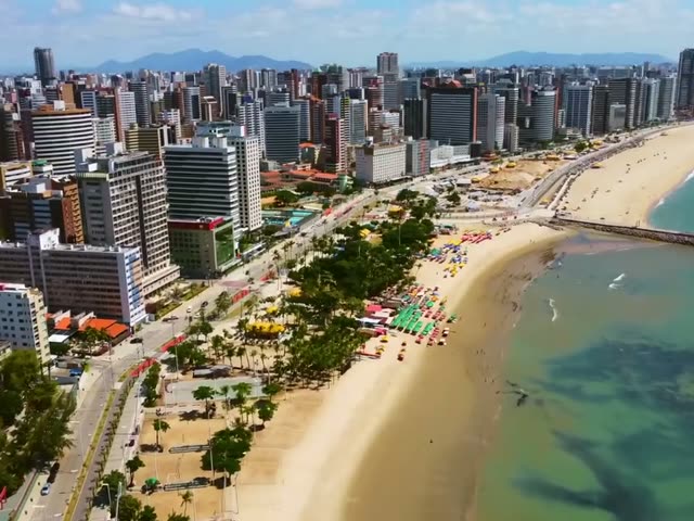 Vista aérea da orla de Fortaleza, com prédios, avenida e faixa de areia