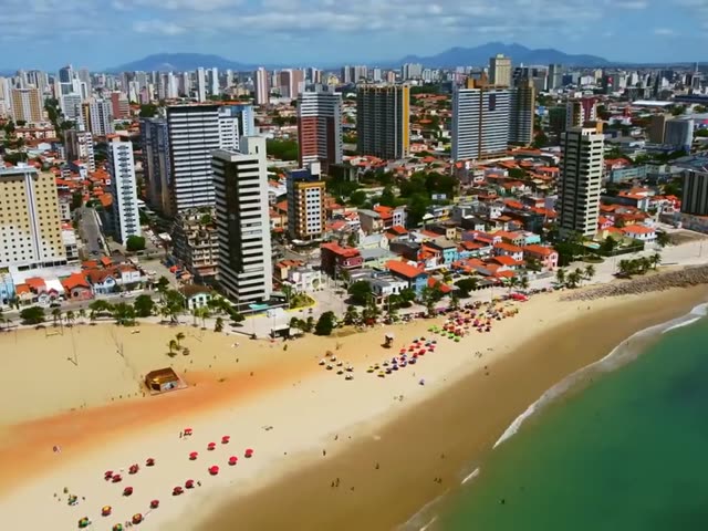 Praia urbana de Fortaleza com guarda-sóis coloridos e bairros ao fundo
